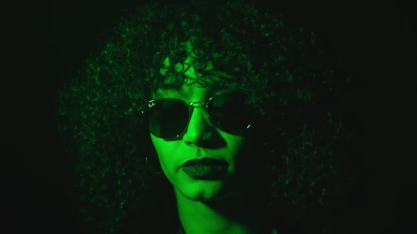 A woman bathed in green light is smoking a cigarette