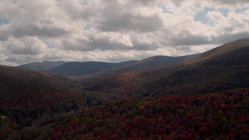 The mountains are covered with trees with heavy clouds moving above