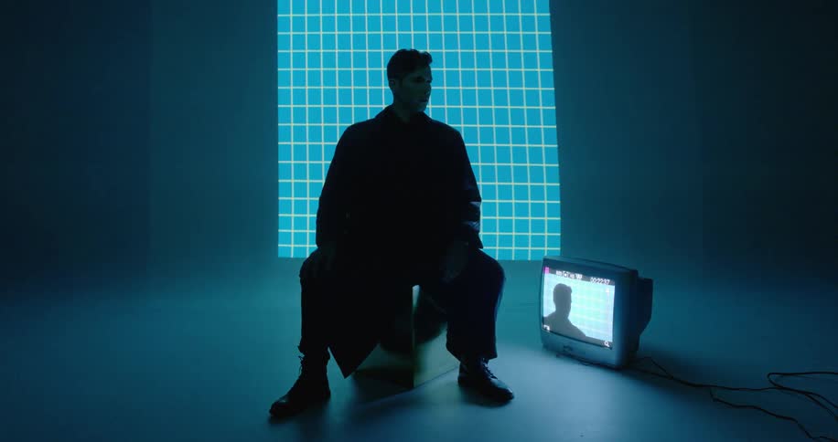A man sits on a cube by a television