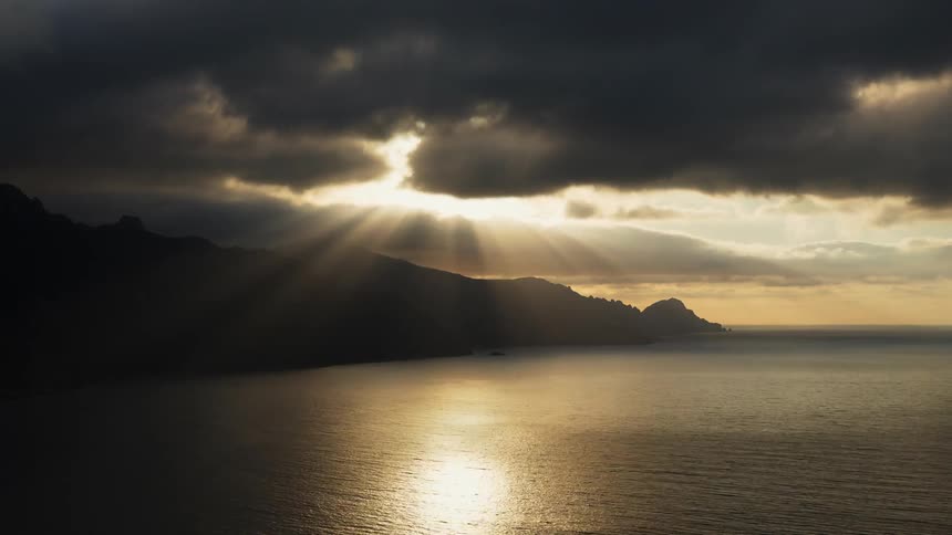 Sun's rays peeking through the clouds at sea and mountains