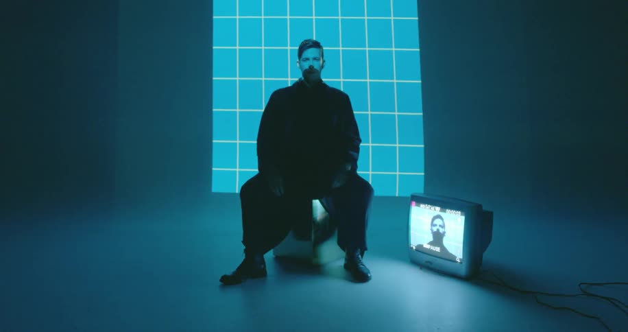 A man sits on a chair in front of a blue and white light grid