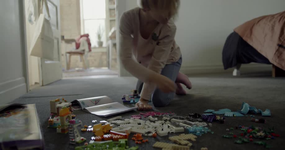 A young girl is playing on the floor with a book and lego-style blocks
