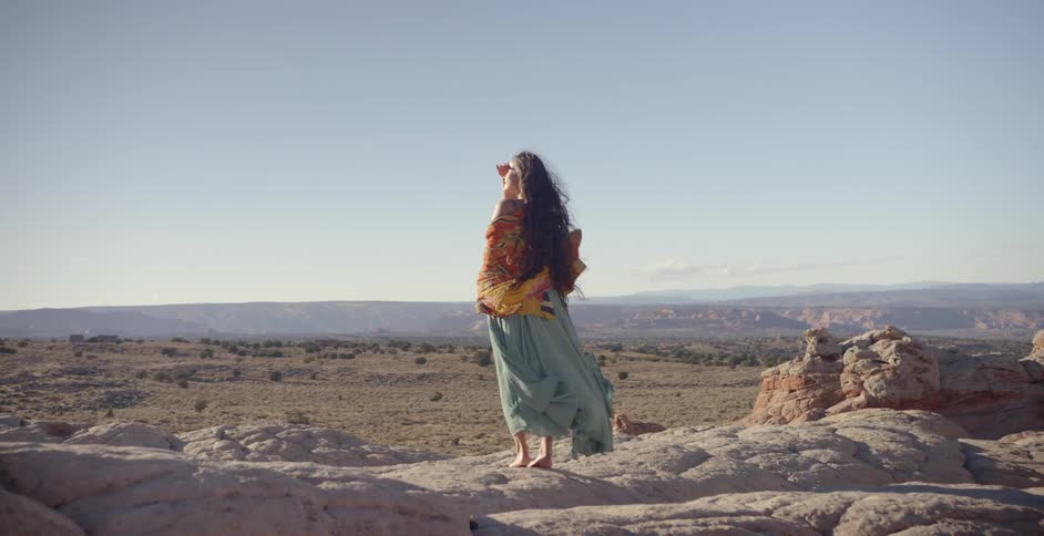 A woman stands atop a rock hill wearing colorful garb