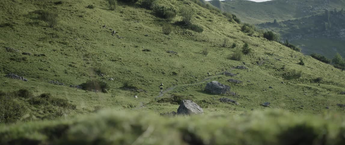 A man is jogging on a dirt path along a hillside during the day