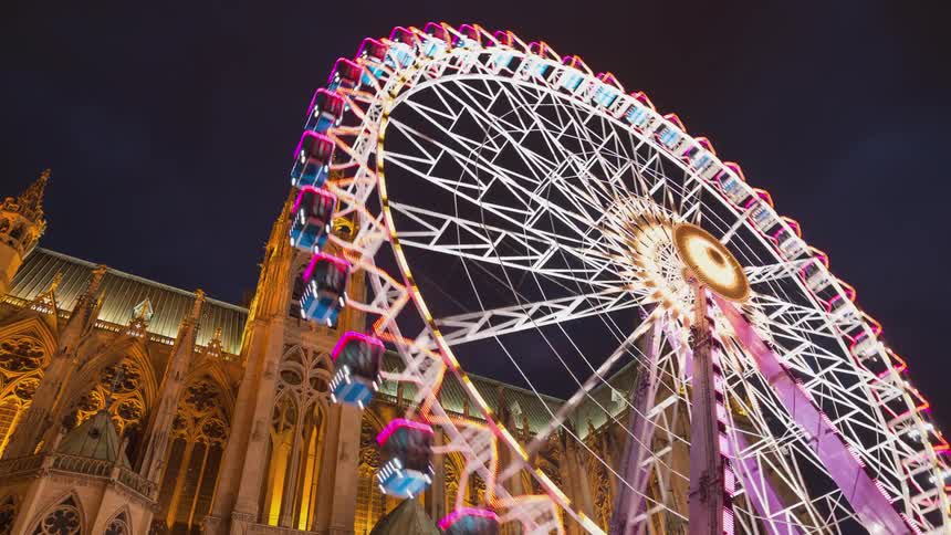 A large ferris wheel turns by a cathedral