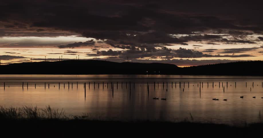 Clouds roll over a fjord at night under golden sky