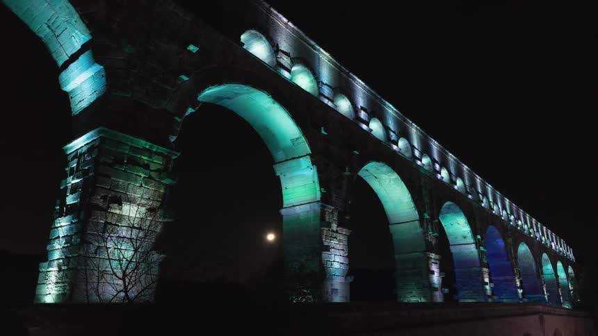 Colored lights play across the Roman Pont du Gard aqueduct at night