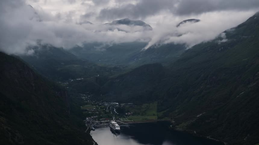 Clouds pass above a fjord with a docked yacht