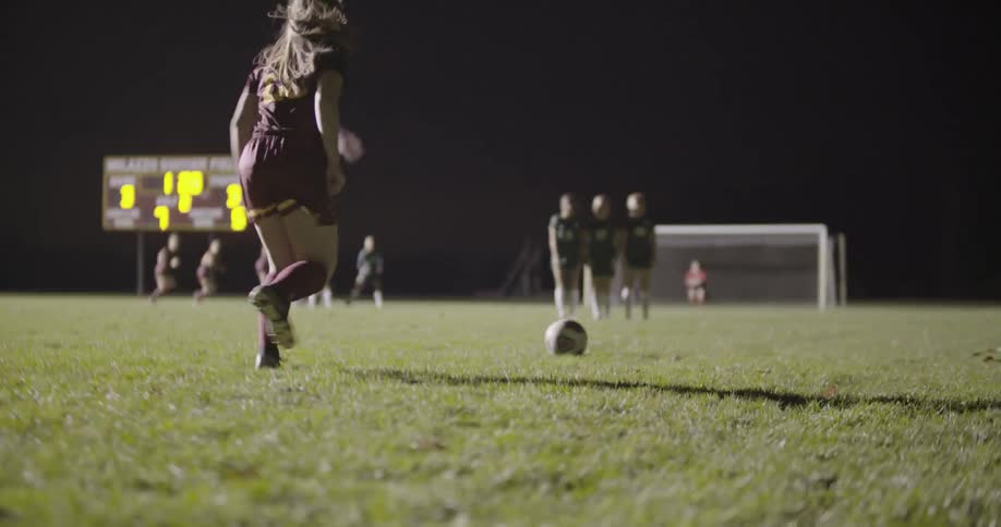 A female soccer player takes a kick in a night game
