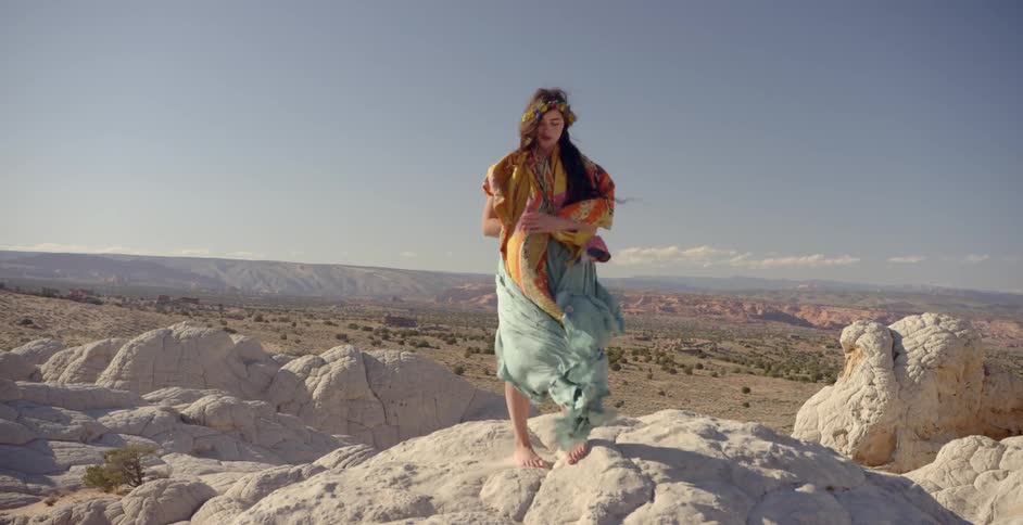 A woman stands on the rocks as her gowns blow in the wind