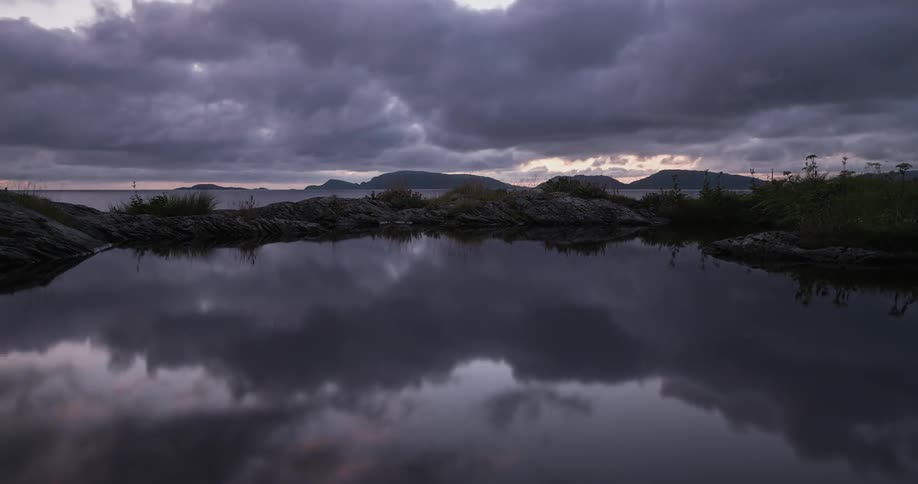 Clouds pass over a calm mountain lake at sunset