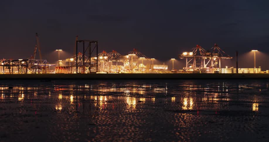 Cranes and vehicles move in a busy shipping port during the night