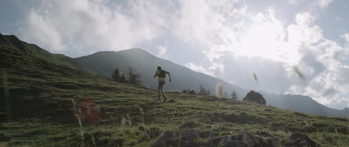 Man jogs up a grassy mountain on a sunny day