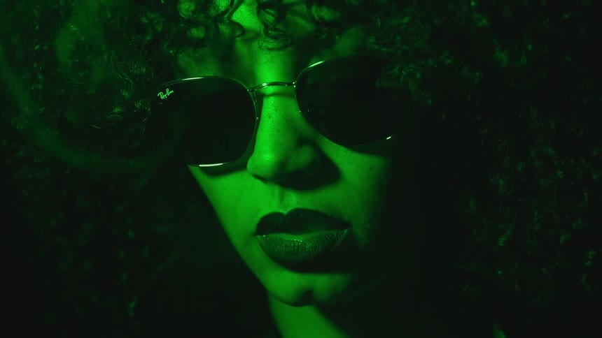 A woman bathed in green light is smoking a cigarette