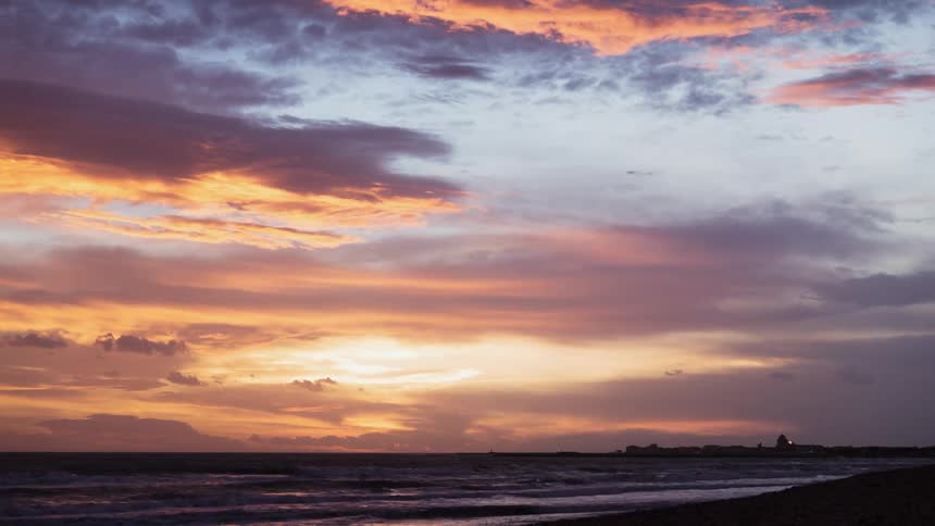 Colorful sunset clouds pass above the flowing ocean water