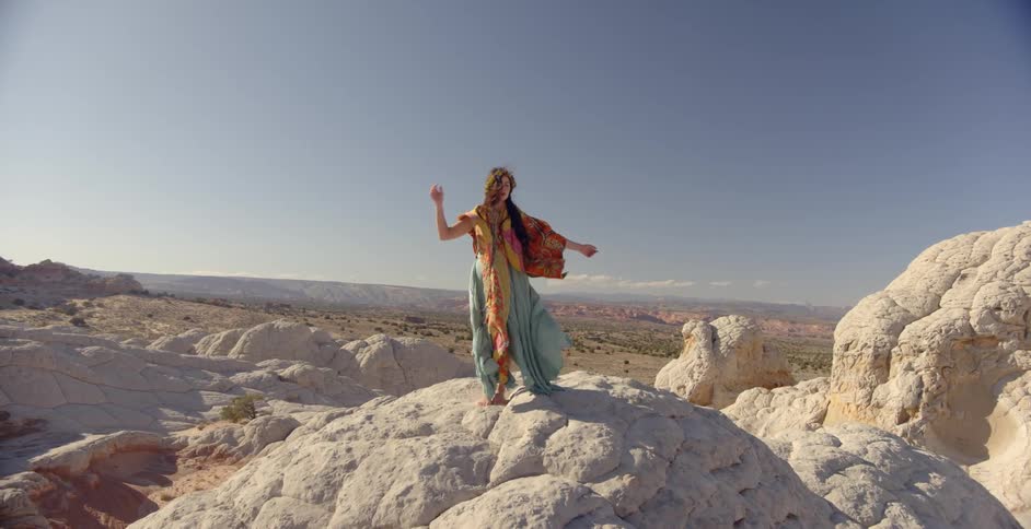 A woman stands atop a rock hill wearing colorful garb