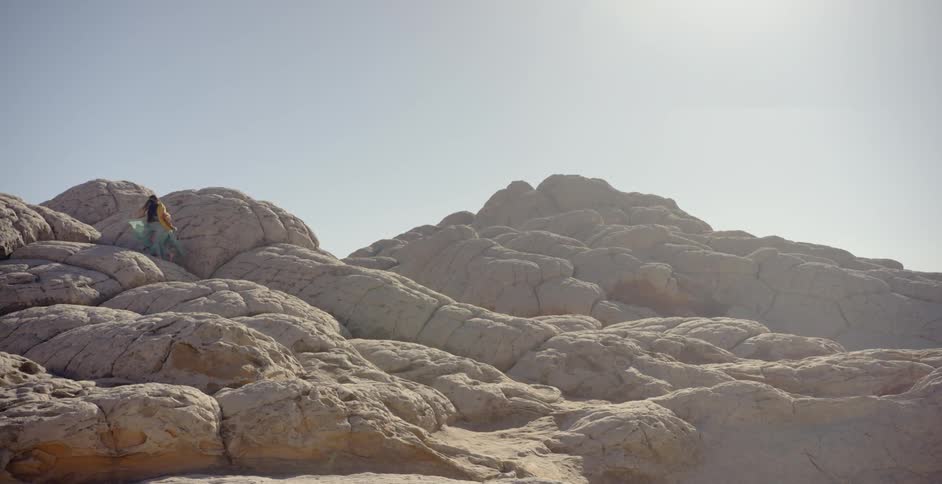 A woman walks on rock formations in the desert on a sunny day