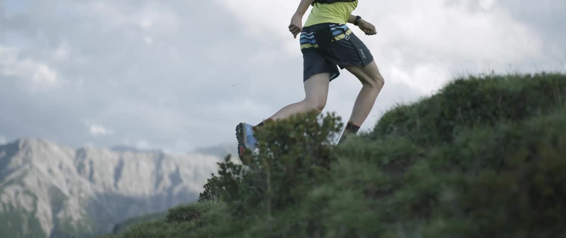 A man is jogging up a steep hill in a mountain range