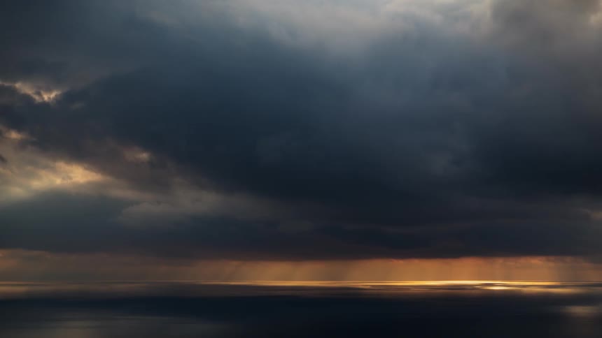 The sun briefly shines in from the heavy clouds onto the water