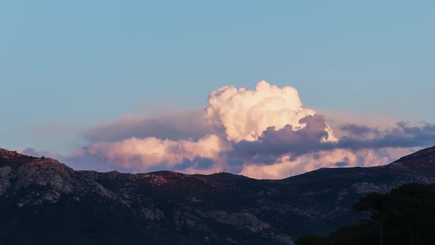 Puffy clouds billowing on top of a mountain at sunset