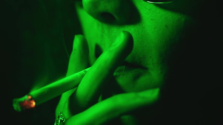 Woman smoking a cigarette illuminated by green light