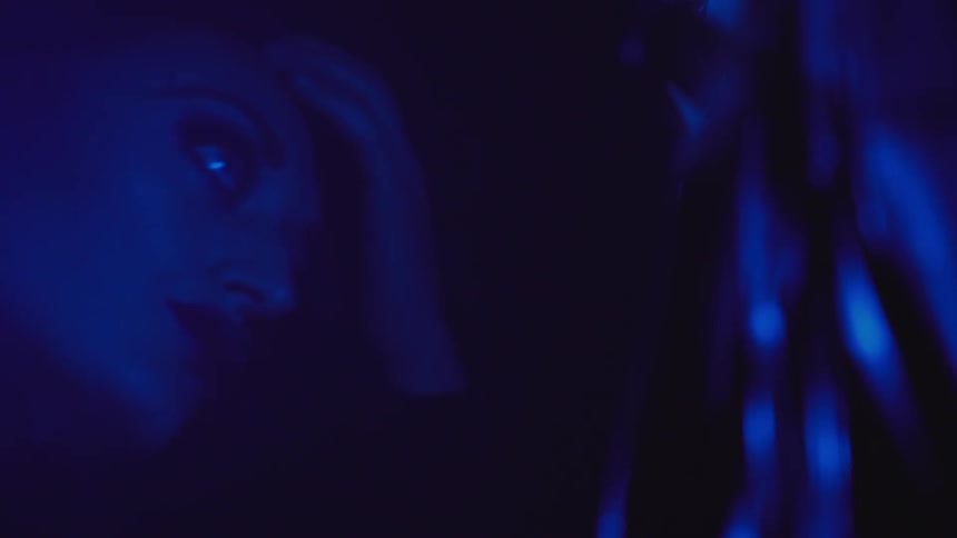 A woman bathed in blue light is looking at herself in a reflective surface