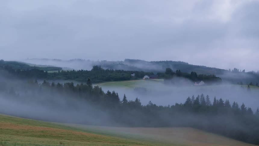 Mist and clouds float over a rural farm landscape