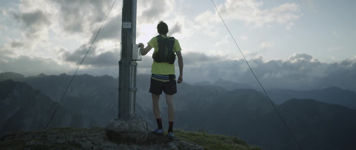 A man jogging and running up to a pole on top of a mountain
