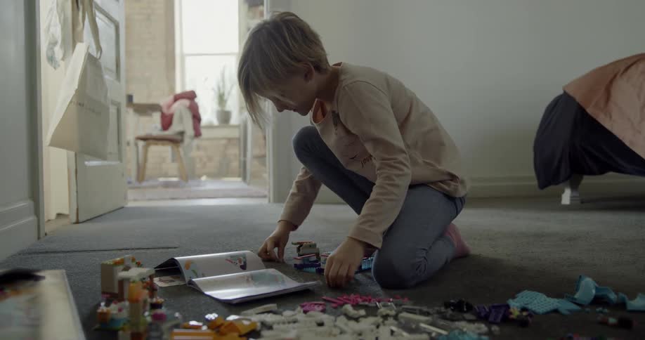 A young girl is playing on the floor with a book and lego-style blocks