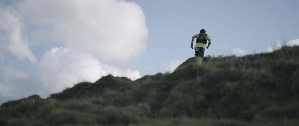 A man runs up a grassy mountainside