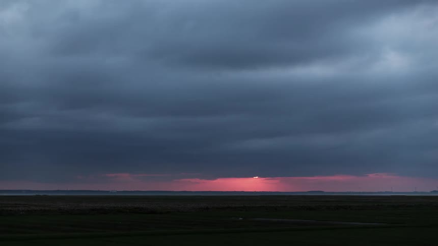 The heavy clouds move over the field at sunset