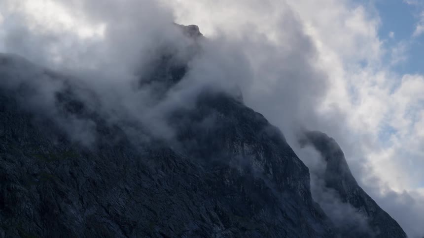 Clouds float and hover around a mountain peak