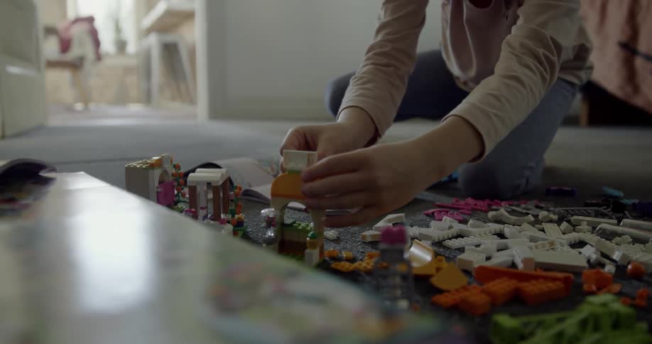 A child playing on the carpet builds a lego wall