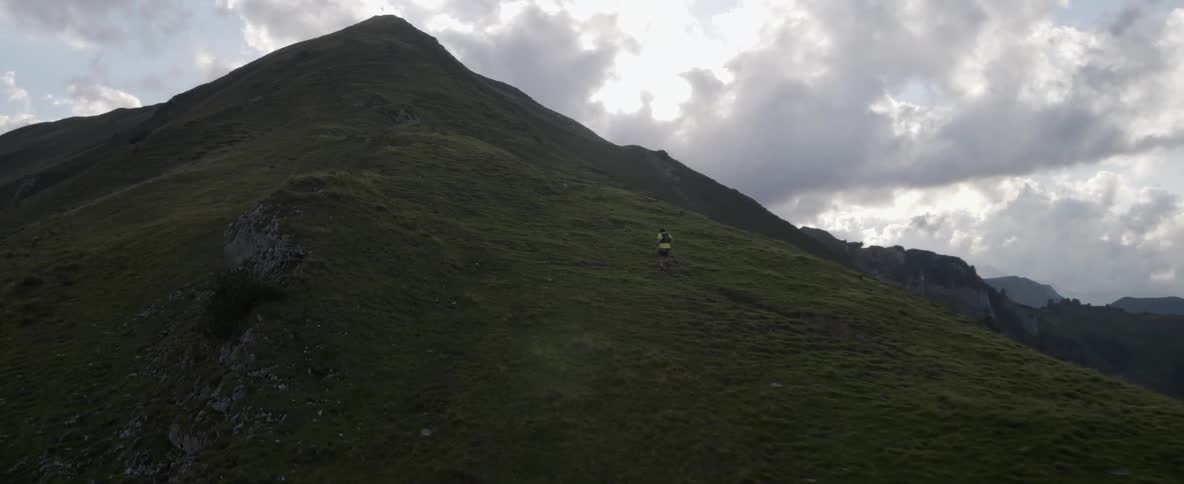 The mountain is tall and green with a person climbing it on a run