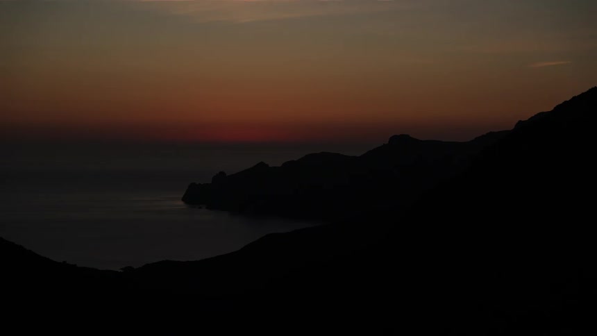 Sun sets over rocky hills by the sea