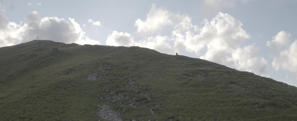 The tall green mountain has a man hiking up in the distance