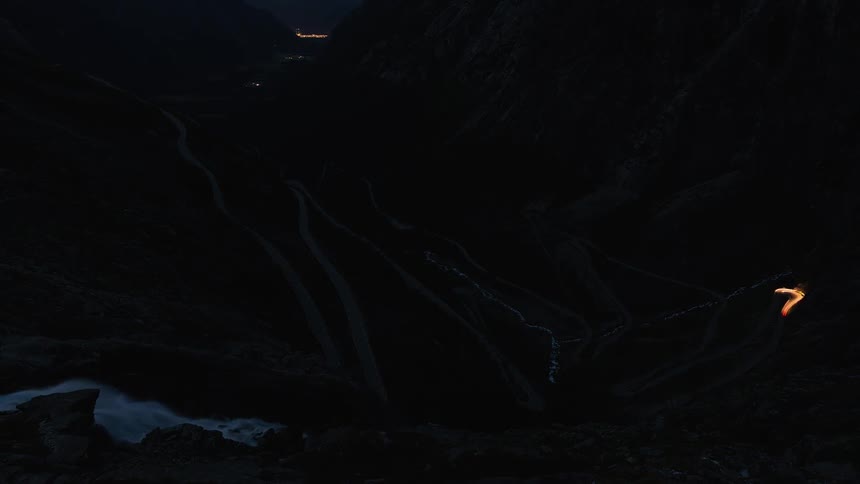 Cars drive on a windy mountain road at night