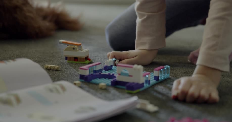 A young girl is creating something with lego-style bricks as she sits on the ground
