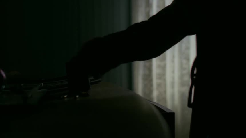 Man holding rifle takes a container of bullets out of top drawer in room