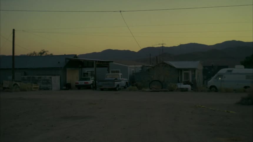 Various vehicles sit parked outside run down buildings during dusk