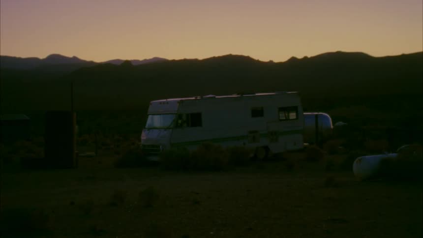 A recreational vehicle is sitting by a hill at dawn