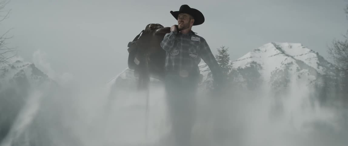 A cowboy carries a saddle on a snow covered field