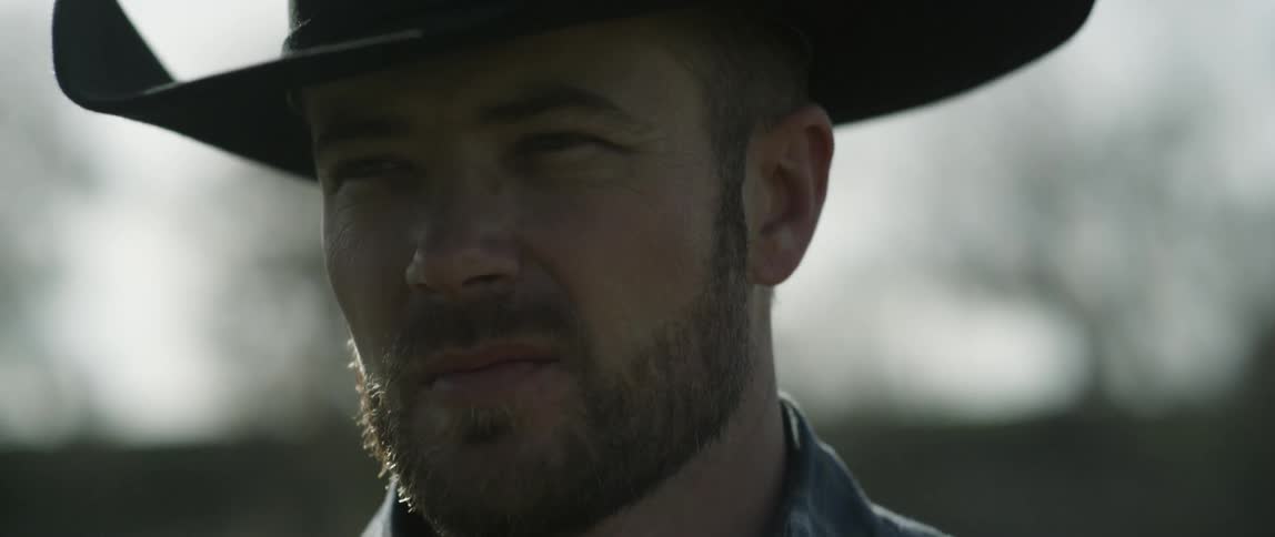 A man wearing a cowboy hat squints into the sun
