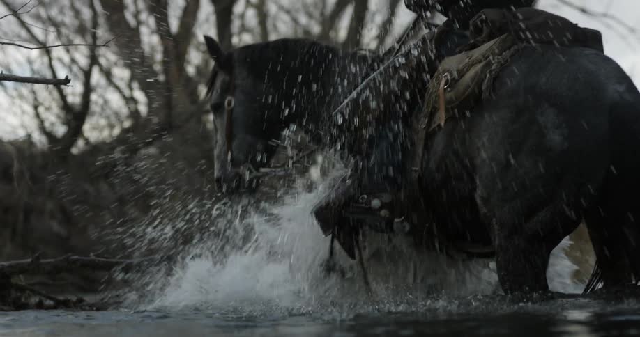 Man riding horse that is splashing it legs in shallow river water