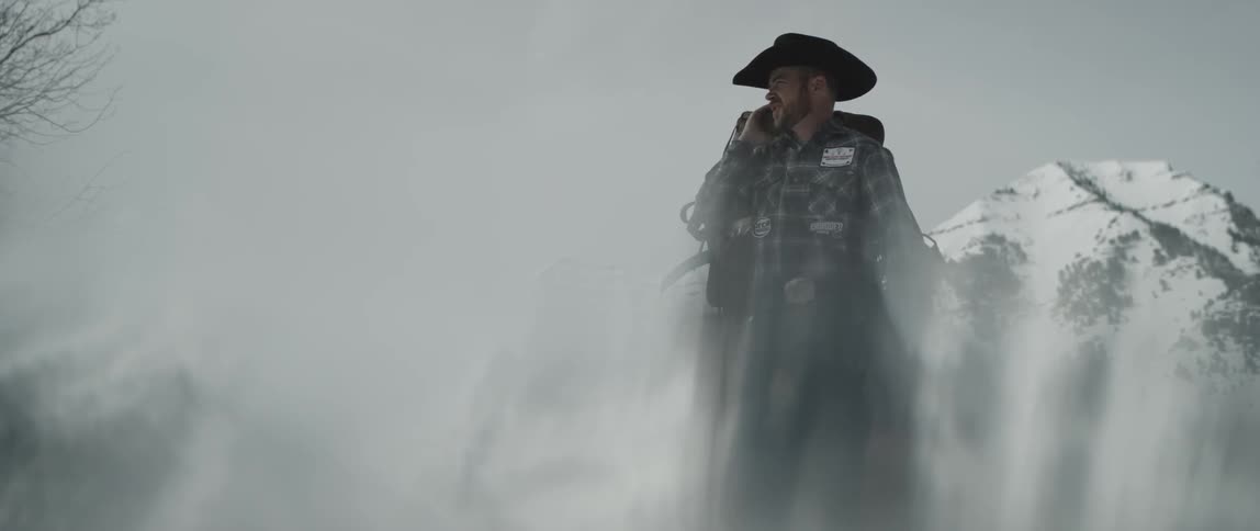Cowboy standing outdoors with a saddle over his shoulder on a cloudy winter day