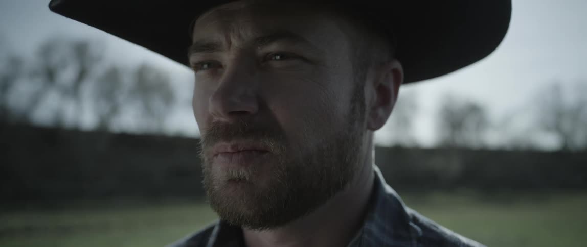 A cowboy stands outside on a sunny day