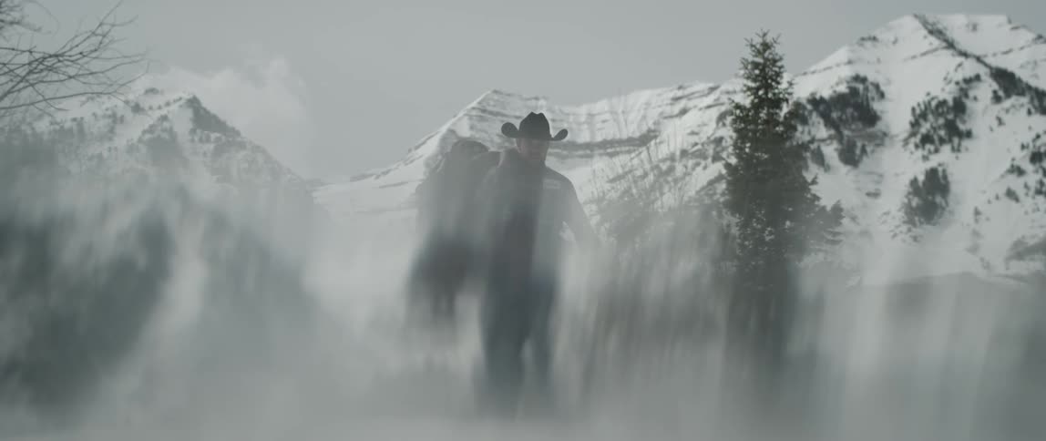 Cowboy carrying a saddle and reins in front of snow covered mountains