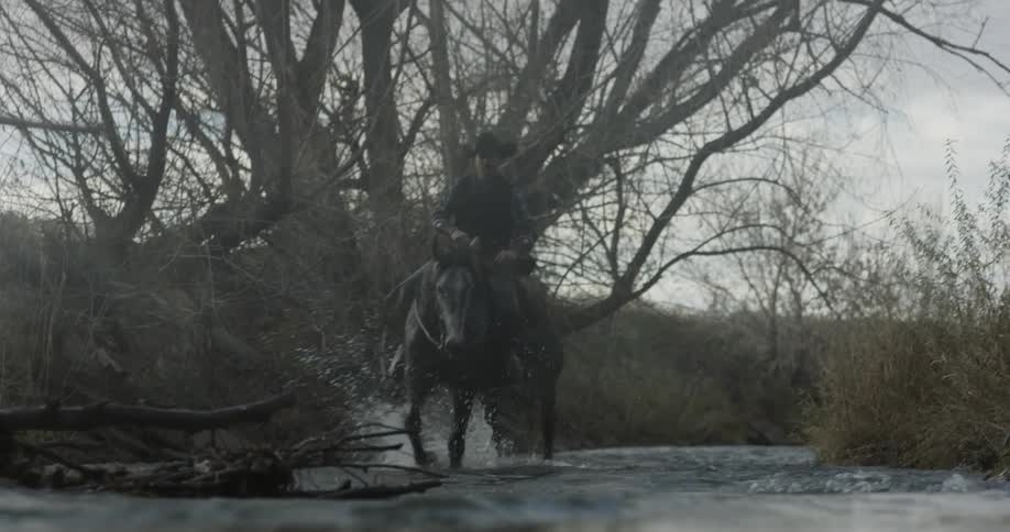 Cowboy riding horse through shallow river water
