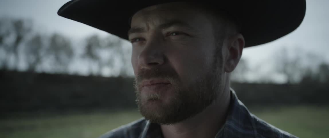 A cowboy stands outside on a sunny day