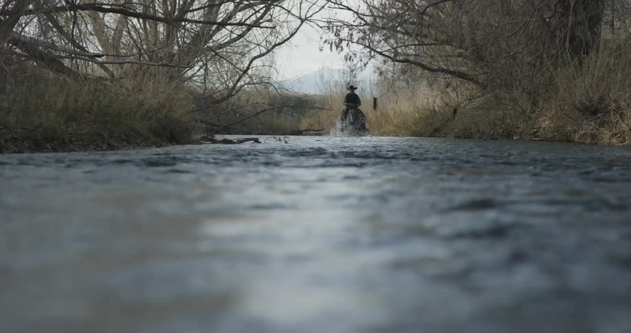 Cowboy riding a horse down a shallow stream on a winter day